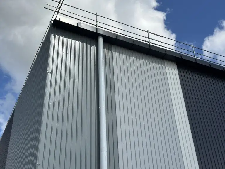 Gutter installation on a commercial metal roof in Brisbane, showing secure downpipe and safety railing system.